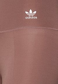 Legíny Adidas v tlumené barvě lila, se hladkým a pružným materiálem, těsným střihem a bílým logem na pase.