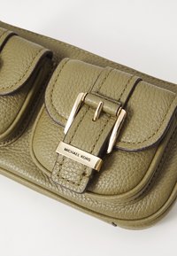 Geantă din piele verde măsliniu cu accesorii aurii, având închidere cu cataramă și două buzunare frontale. Material texturat cu accente de cusătură.