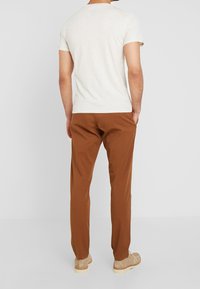 Lichtbeige t-shirt met korte mouwen gecombineerd met een paarse broek, met een ontspannen pasvorm. De stof lijkt zacht met een gladde textuur.