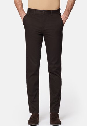 Brązowe spodnie w slim fit, wykonane z gładkiego materiału. Posiadają zapięcie na guzik i kieszenie z przodu. Noszone z beżową bluzką i brązowymi butami.