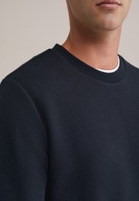 Sweatshirt texturat de culoare bleumarin, cu guler rotund și manșete ribbed, având un model subtil și un finisaj moale, țesut.
