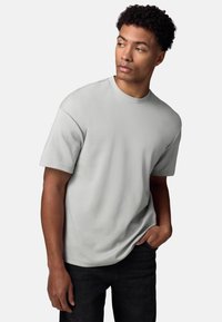 Lys grå kortærmet t-shirt, rund hals, afslappet pasform, blød tekstur. Båret med mørke jeans, stående mod en ensfarvet baggrund.