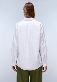 Camicia bianca a maniche lunghe con colletto abbottonato, vestibilità sartoriale, orlo curvo e spacchi laterali. Realizzata in tessuto liscio, presenta cuciture e dettagli minimi.