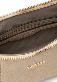 Beige leather bag interior with gold zipper, featuring multiple compartments and a textured lining. Logo embossed inside.