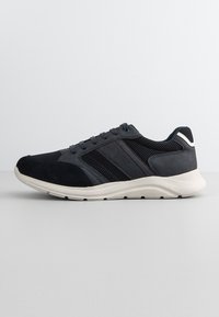 Sneaker in rete e camoscio neri e grigi scuri con suola ammortizzata bianca, chiusura con lacci e striscia riflettente sul tallone.