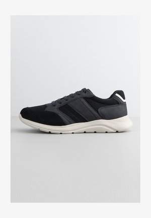 Sneaker in rete e camoscio neri e grigi scuri con suola ammortizzata bianca, chiusura con lacci e striscia riflettente sul tallone.