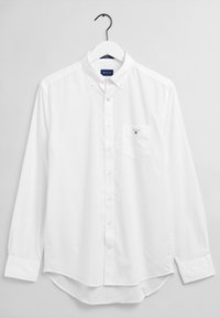 Chemise blanche à boutons avec col, manches longues et poche poitrine. Présente un petit logo sur la poche et une texture lisse.