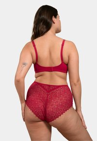 Soutien-gorge en dentelle rouge et culottes taille haute. Le soutien-gorge a des bretelles réglables et une fermeture à crochets. Les culottes présentent une bordure en dentelle festonnée et un motif géométrique.