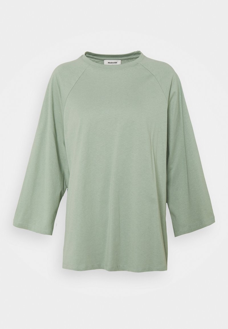 Haut ample à manches longues vert clair avec encolure ronde et manches raglan, présenté sur fond blanc.