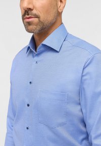 Lys blå button-down skjorte med et tekstureret mønster, spidse kraver og en brystlomme. Inkluderer mørkeblå knapper og en skræddersyet pasform.