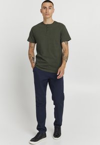 Mørkegrøn kortærmet henley skjorte med tre knapper, kombineret med marineblå lige bukser og sorte høj-top sneakers.