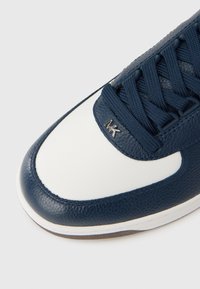 Αθλητικό παπούτσι από δέρμα σε ναυτικό μπλε χρώμα με λευκή μύτη, υφή στην επιφάνεια, ραφές και ασημένιο λογότυπο. Κορδόνια σε ταιριαστό ναυτικό μπλε χρώμα.