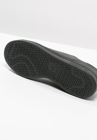 Svart gummisul med hexagonalt mönster, med en slät kant och subtil branding. Texturen är grov, vilket ger bra grepp.