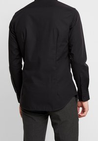 Svart långärmad skjorta med en slät textur, rundad fåll och knäppte ärmslut. Har en klassisk krage och minimalistisk design.