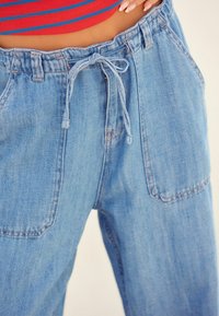 Jasnoniebieskie dżinsowe spodnie z elastycznym pasem, regulowanym sznurkiem i dwoma przednimi kieszeniami. Charakteryzują się luźnym krojem i miękką fakturą.