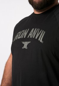 Černé tričko s šedým potiskem "IRON ANVIL" a grafikou kovadliny. Vyrobeno z měkké tkaniny s hladkou strukturou a krátkým rukávem.
