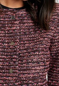 Veste texturée avec un motif tissé multicolore dans des teintes de rose, marron et marine, dotée de boutons métalliques sur le devant.