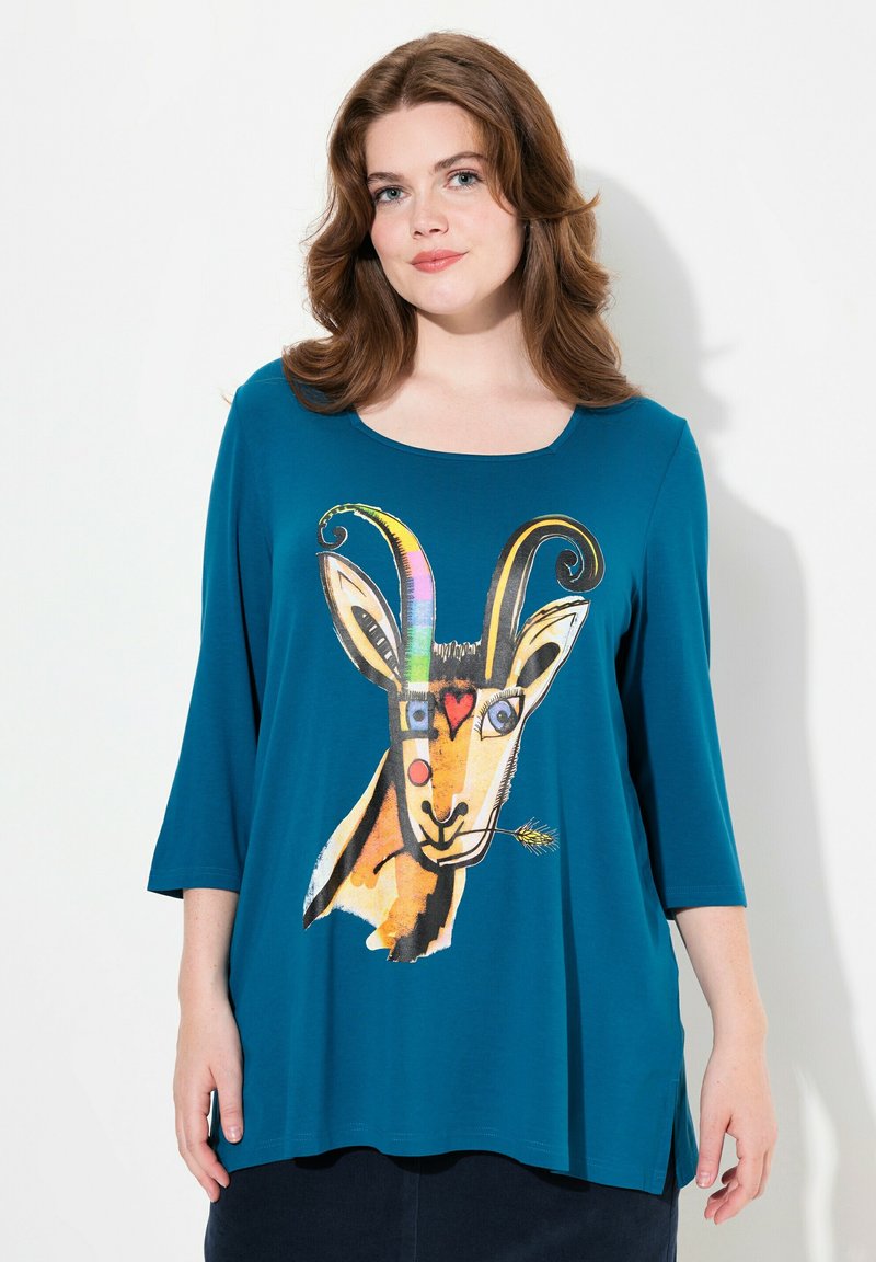 Türkise, oversized Bluse mit rundem Halsausschnitt und Dreiviertelärmeln, die ein buntes Ziegenmotiv auf der Vorderseite zeigt.