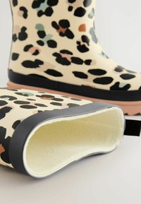 Bottes de pluie en caoutchouc à imprimé léopard avec une base crème, des accents noirs et une doublure douce et texturée. Elles disposent d'une languette à l'arrière.