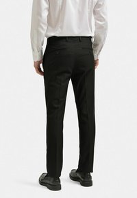 Svarta byxor i slätt tyg med rak passform, två bakfickor med knäppningar och parat med svarta skor.