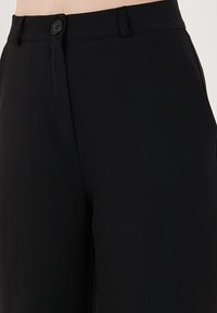 Pantaloni negri dintr-un material neted, cu un talie ajustată, închidere cu nasture și detalii de pliuri, concepuți pentru o potrivire ajustată.