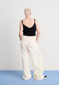 Black knitted crop top with spaghetti straps paired with wide-leg, cream-colored pants in textured fabric. Model stands with back to the camera.