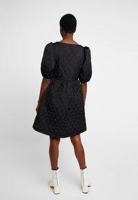 Schwarzes gesteppte Kleid mit tailliertem Schnitt, gepufften Ärmeln und schwingendem Rock, aus einem glatten Stoff mit dezentem Glanz gefertigt.