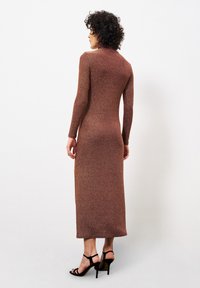 Rosenholz schimmerndes Strickkleid mit langen Ärmeln, figurbetontem Design und bodenlanger Schnittführung. Stiletto-Absätze ergänzen den Look. Glatte Textur.