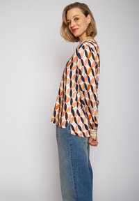 Koszula z długim rękawem wykonana z gładkiego materiału, z geometrycznym wzorem w pastelowym pomarańczy, granacie i turkusie na kremowym tle.