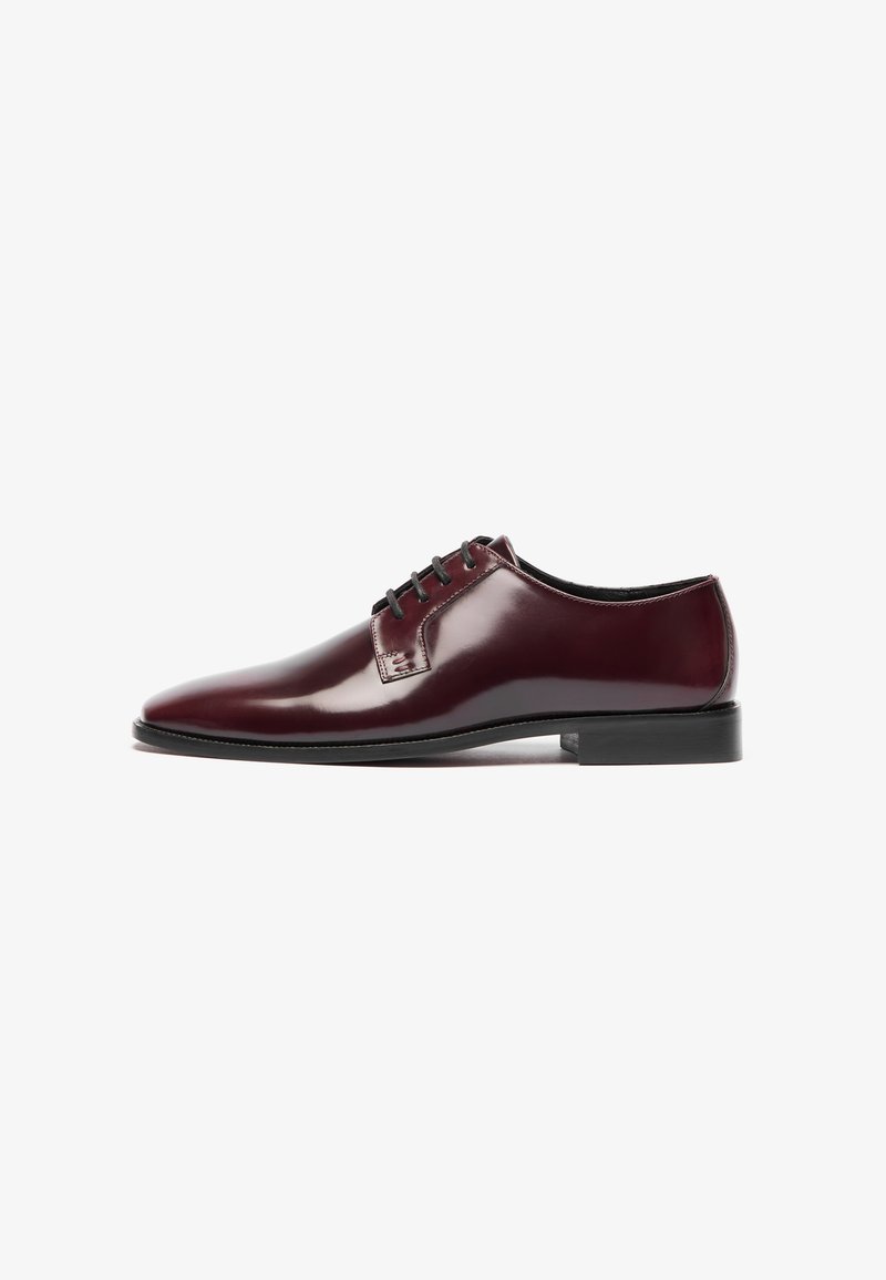 Zapato de vestir de cuero burdeos con un acabado suave, punta afilada, cinco ojetes para los cordones y un tacón bajo negro.