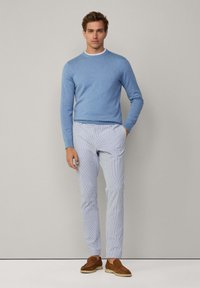 Jasnoniebieski sweter z dzianiny, z białym kołnierzykiem, w połączeniu z pasiastymi, jasnoniebieskimi spodniami oraz brązowymi zamszowymi butami slip-on. Gładki materiał, luźny krój.