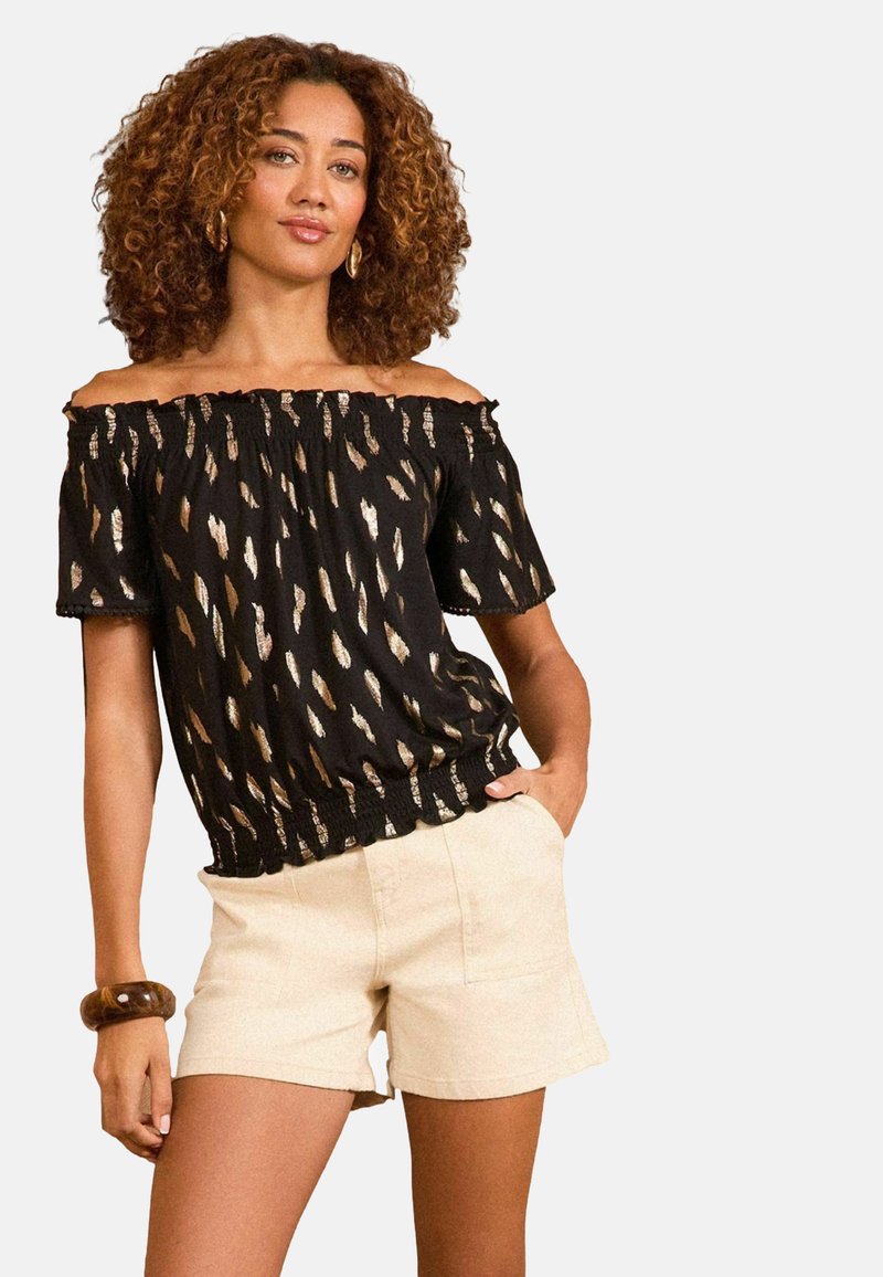Juodas off-the-shoulder viršus su auksiniu abstrakčiu raštu, sutraukta iškirpte ir elastingu juosmeniu, derinamas su šviesiais smėlio spalvos šortais.