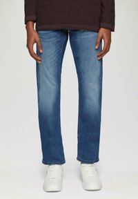 Jeans en denim bleu clair avec une coupe droite, présentant un lavage délavé et des whiskers subtils. Associés à des baskets blanches pour créer un contraste.