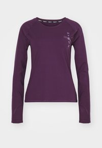 Fioletowa koszulka sportowa z długim rękawem i okrągłym dekoltem, z subtelnym detalem logo po lewej stronie oraz gładką, elastyczną teksturą.