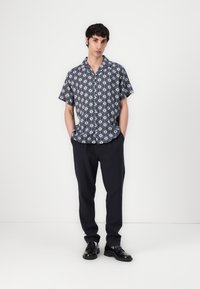 Camicia a maniche corte, blu navy con motivi floreali bianchi, abbinata a pantaloni scuri e scarpe nere, che mostra una vestibilità rilassata e uno stile casual.