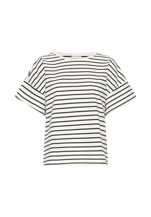 Femme debout à l'intérieur portant un haut à manches courtes rayé blanc et noir, un jean bleu clair et des ballerines beige avec des taches noires.