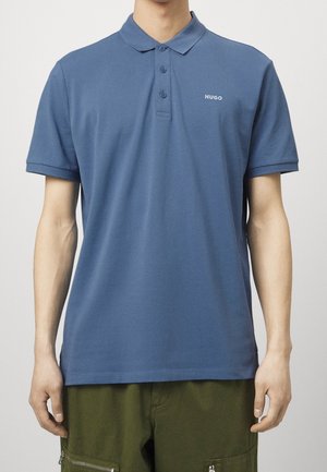 Niebieska koszulka polo wykonana z bawełny, z klasycznym kołnierzykiem, trzema guzikami oraz małym białym logo na lewej piersi. Krótkie rękawy.