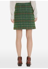 Vihreä ruudullinen hame ruskeilla yksityiskohdilla, valmistettu teksturoidusta kankaasta. Takana vetoketju, pituus polven yläpuolella, yhdistetty ruskeisiin nilkkureihin.
