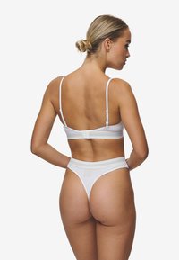 Bralet alb cu bretele înguste și închidere cu cârlig; thong asortat cu un tiv moale și acoperire minimă; textură netedă.