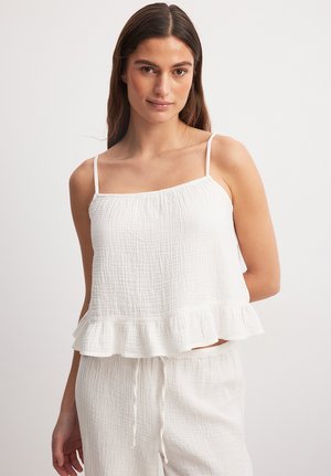 White, sleeveless top with a textured fabric and a ruffled hem, featuring thin straps and a relaxed fit. Paired with matching light pants.