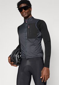 Mustra mustraga vesti musta kõrgkraega, lukuga rinnanäppu ja kontrastsetes varrastes. Ülikitsad mustad lühikesed püksid ümmarguse pehmenduste detailiga.