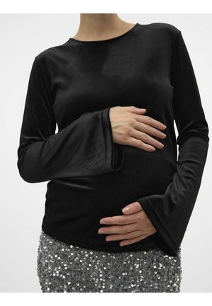Persoon die een zwart top met lange mouwen en een paillettenrok draagt, houdt voorzichtig de handen op een ronde buik, wat op zwangerschap wijst.