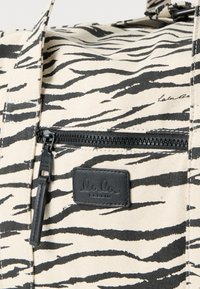 Τσάντα από καμβά με κρεμ φόντο και μαύρες ρίγες τίγρη. Διαθέτει μαύρη τσέπη με φερμουάρ και δερμάτινο λογότυπο με την επιγραφή "lala BERLIN".