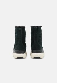 Gröna mocka ankstövlar med en kort pälskrage, med en svart gummisula och präglad "SOREL"-logotyp på hälen.