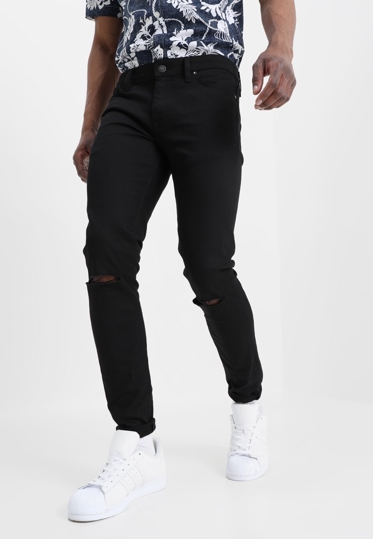 Svarta slitna skinny jeans med revor vid knäna, kombinerade med en blommönstrad skjorta och vita sneakers med snäckformad tådesign.