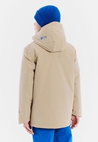 Beige geïsoleerde jas met capuchon, met een blauw logo op de achterkant. Gecombineerd met blauwe onderkleding, met een zachte textuur en een eenvoudig ontwerp.