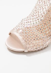 Zapato de tacón abierto en satén de color rosa claro, con un diseño de malla adornado con cuentas iridiscentes y de colores claros.