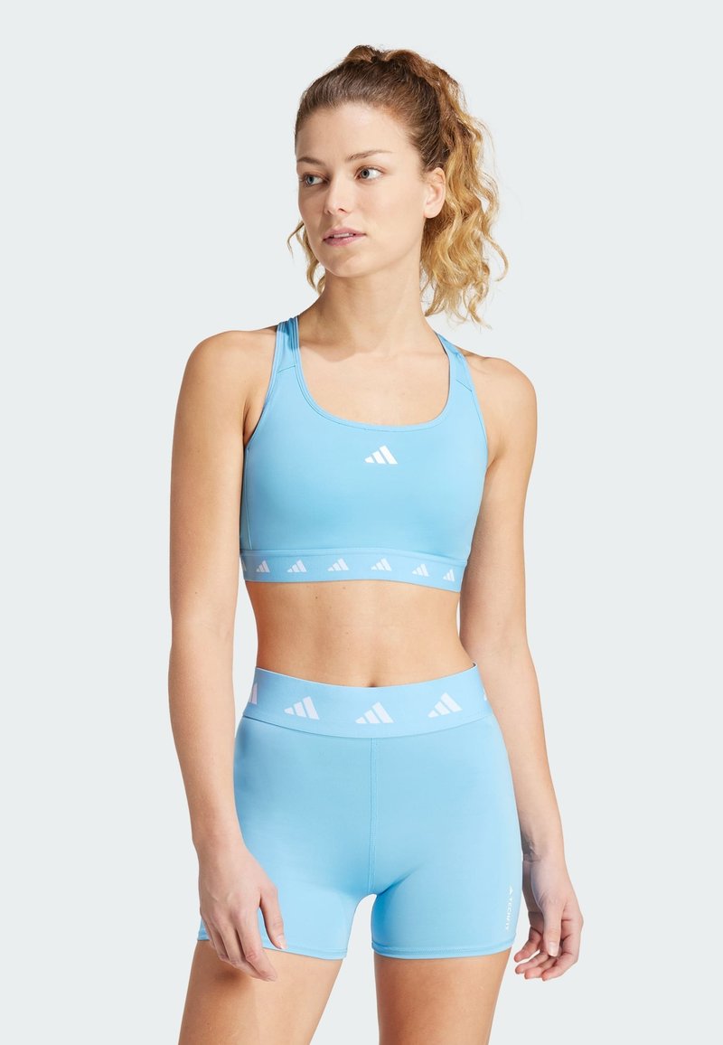 Sujetador deportivo de color azul claro y pantalones cortos a juego, fabricados con una tela suave y elástica, que presenta acentos de logo blanco repetidos en la banda.