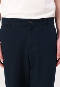 Navy blue trousers with a smooth texture, featuring a button closure, belt loops, and a classic fit. No visible patterns or accents.