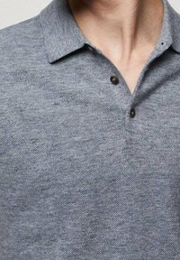 Polo gris en tissu texturé avec un col, comprenant deux boutons foncés au cou et un design simple et épuré.